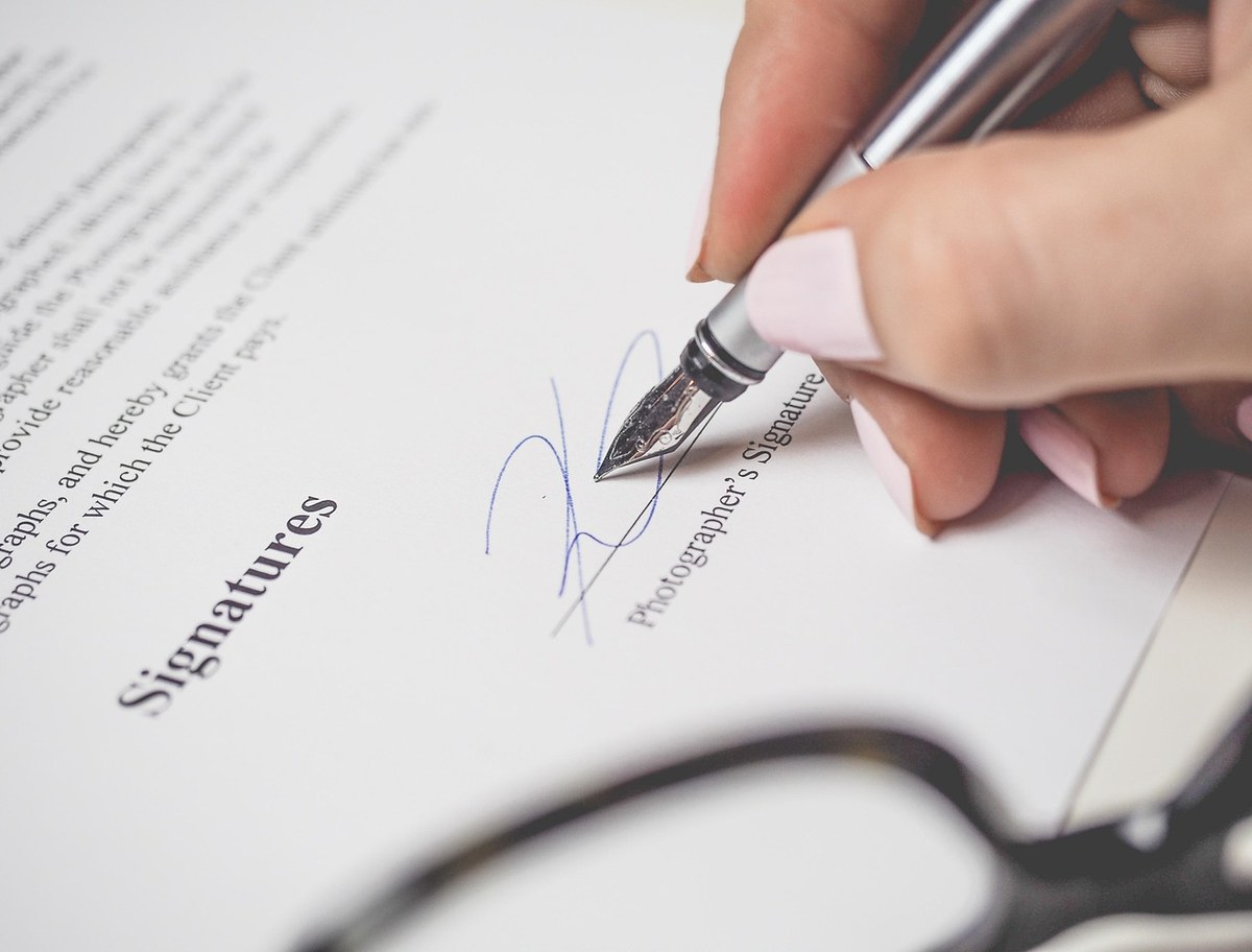 Hand unterschreibt einen Vertrag mit einem Füller auf hellem Papier